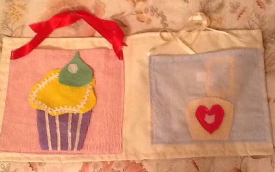 Two buns with felt shapes to create muffins.  Velcro fastenings.  Shapes are stored in the apron  pockets, behind the bun, then fasten the ribbon straps.  Materials: cotton fabric, felt, ribbon, Velcro 
